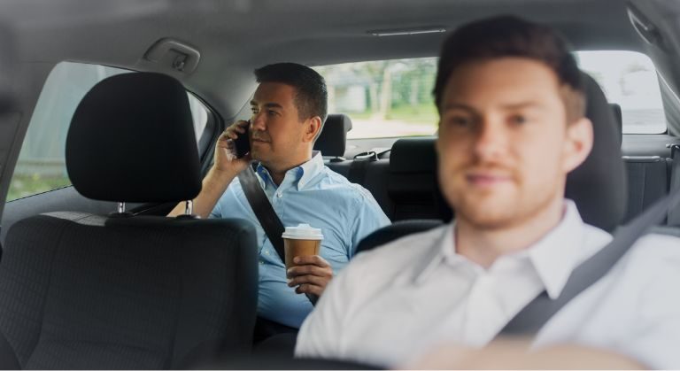 Chofer conduciendo y cliente haciendo una llamada dentro de un vehículo